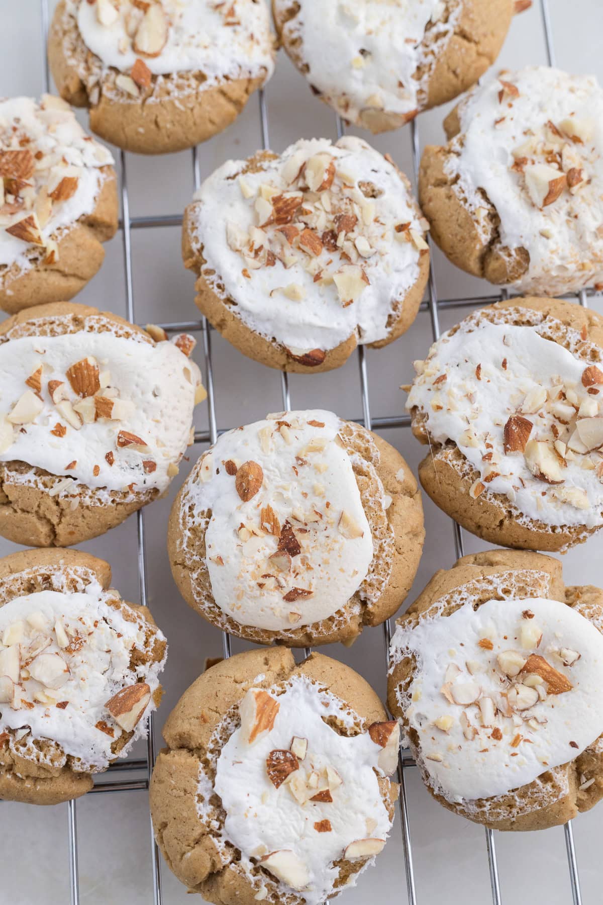 Cookies topped with white icing and chopped almonds arranged on a cooling rack.
