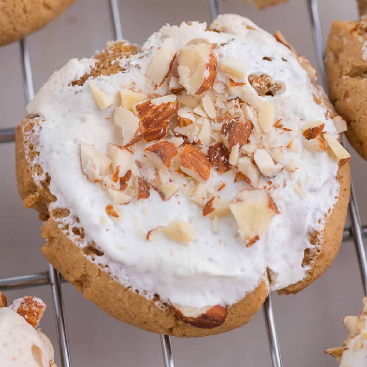 A cookie topped with white icing and chopped nuts sits on a metal cooling rack.