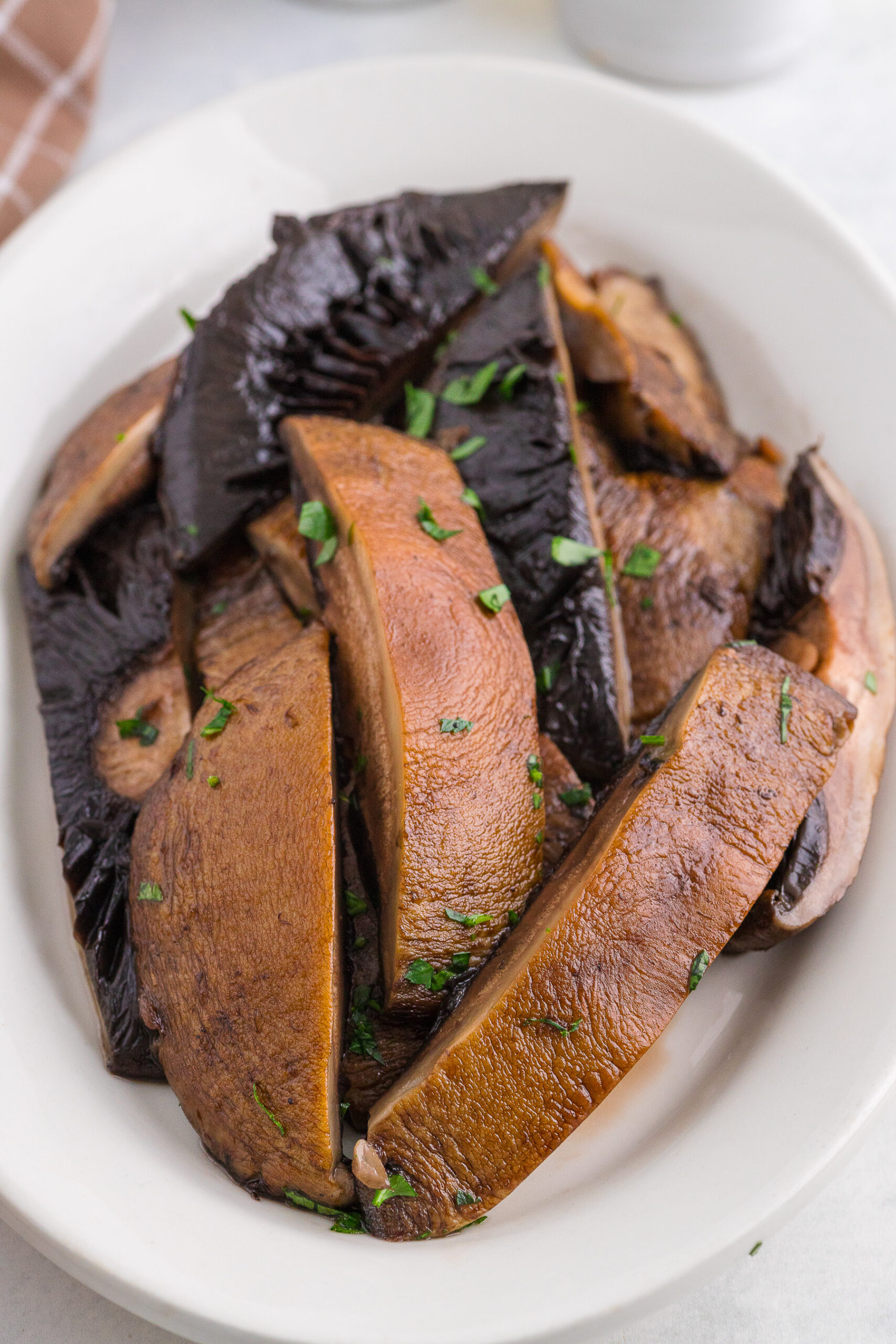 Sliced, cooked portobello mushrooms garnished with chopped parsley on a white oval plate.