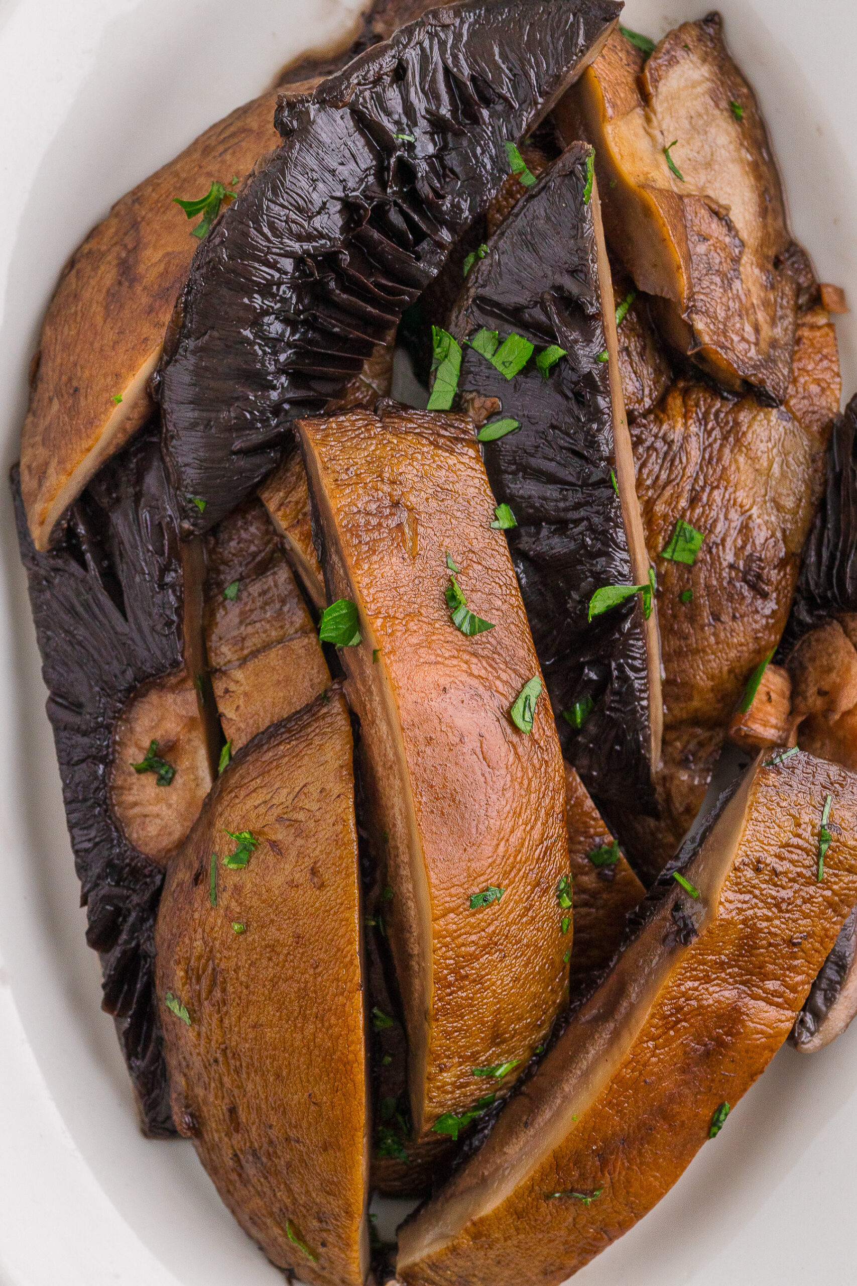 Sliced, cooked portobello mushrooms garnished with chopped fresh herbs on a white plate.