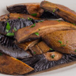 Sliced cooked portobello mushrooms garnished with chopped parsley on a white plate.