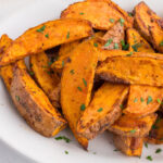 A plate of baked sweet potato wedges garnished with chopped herbs.