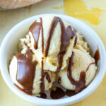 A white bowl filled with three scoops of vanilla ice cream, topped with chocolate syrup drizzle.