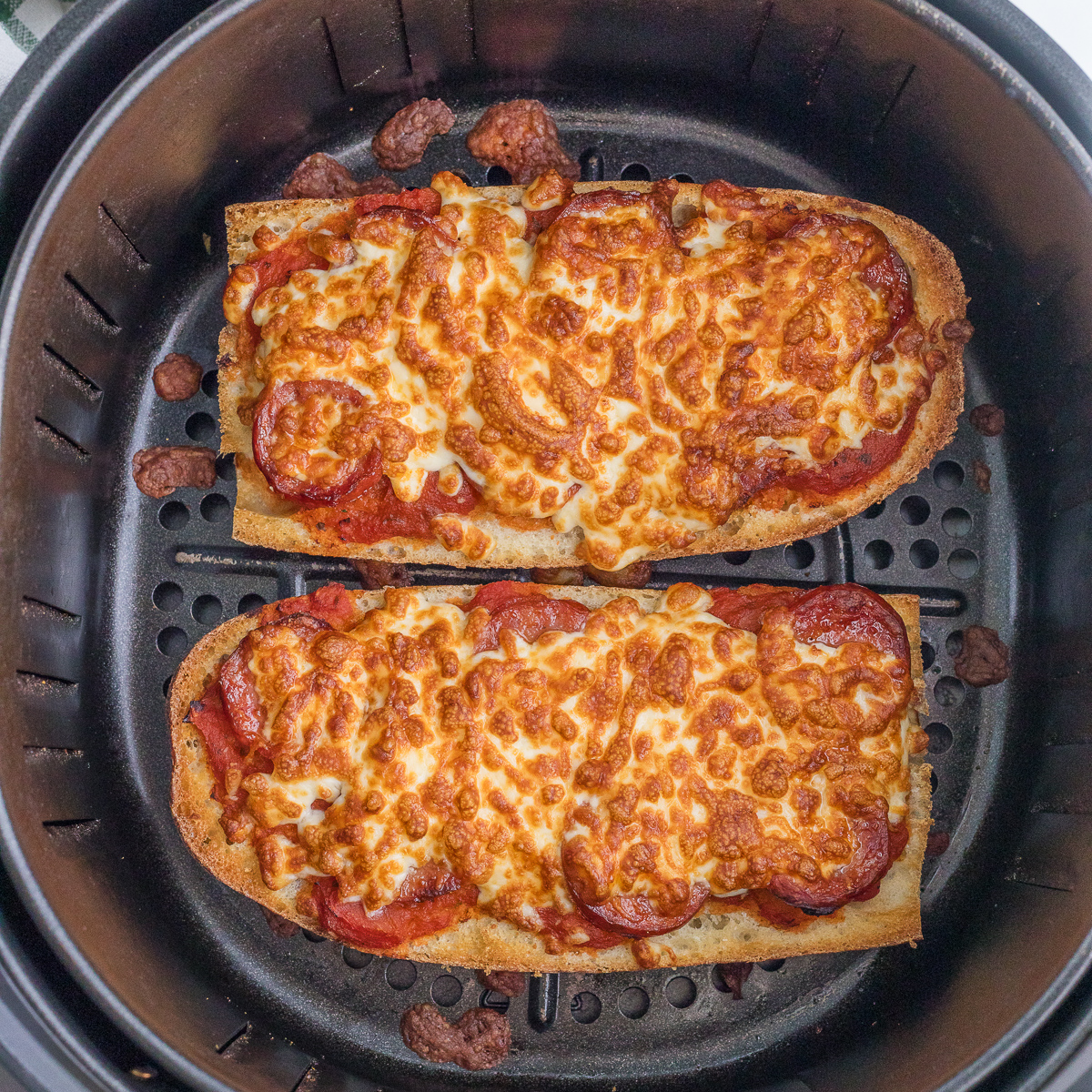 Two slices of French bread topped with melted cheese and pepperoni are cooked inside an air fryer basket.