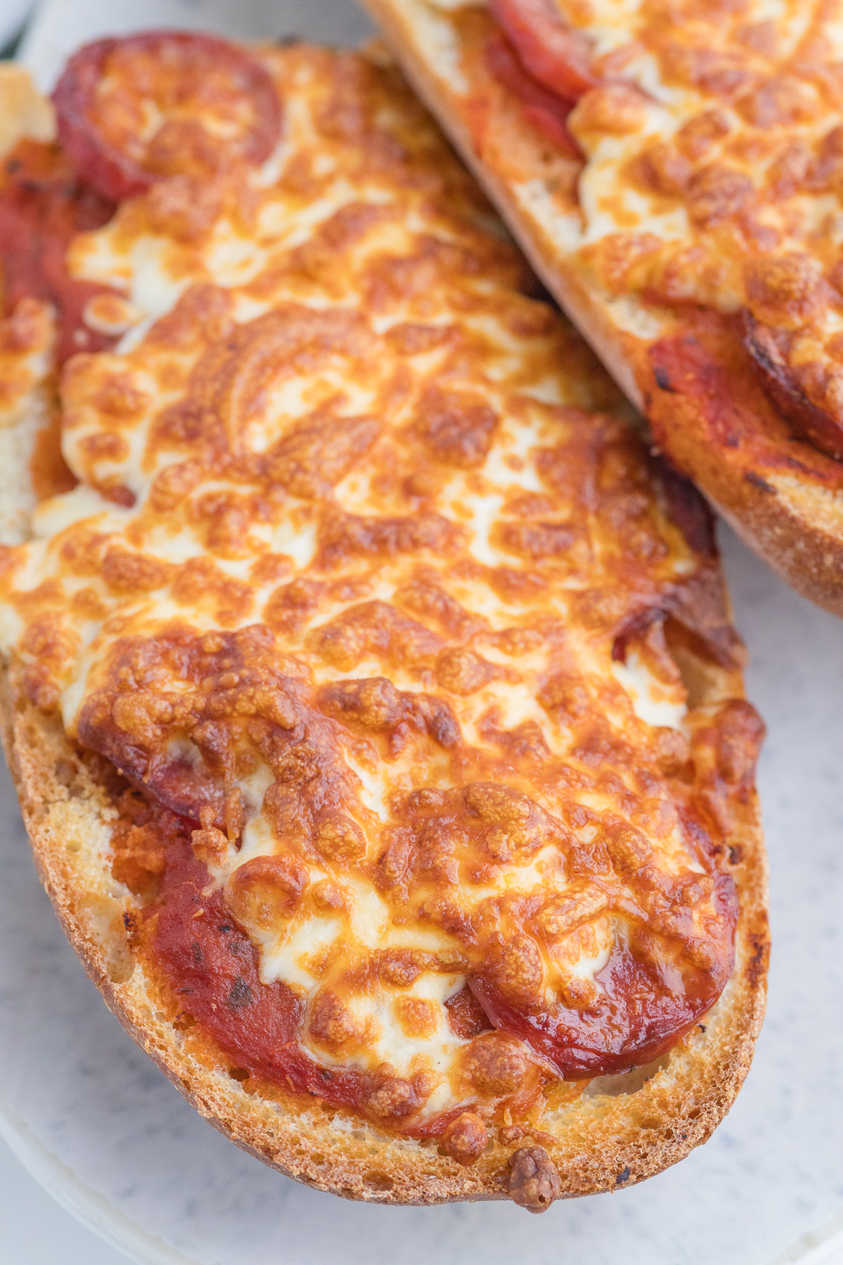 Close-up of two pieces of French bread pizza topped with melted cheese and tomato sauce on a white plate.