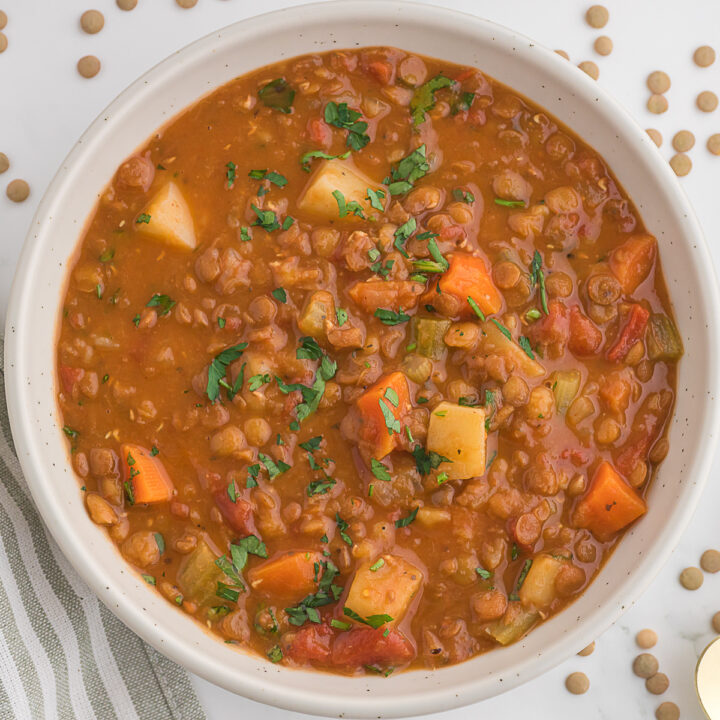 A bowl of lentil soup with diced potatoes, carrots, celery, tomatoes, and parsley, viewed from above.