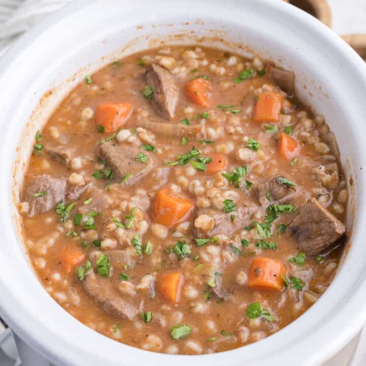 Beef and barley stew with carrots and parsley in a white ceramic bowl.