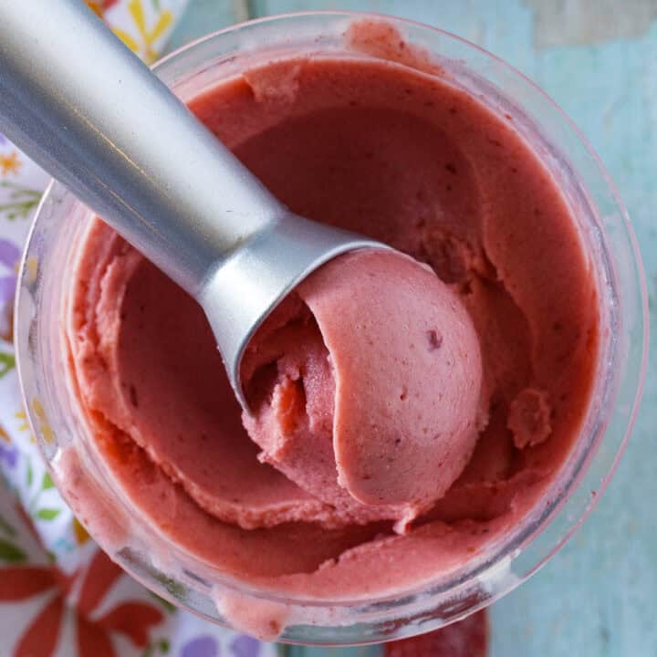 A metal ice cream scoop in a container of bright pink ninja creami strawberry ice cream with smooth texture and swirls.